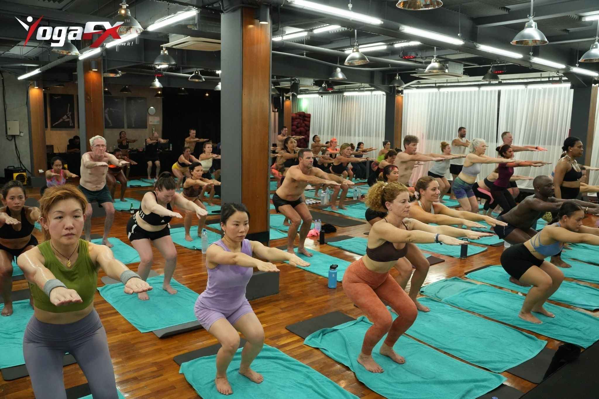 Students in a humid 40°C room holding Half Moon Pose together during the fixed standing series of a 90-minute 26 and 2 hot yoga class