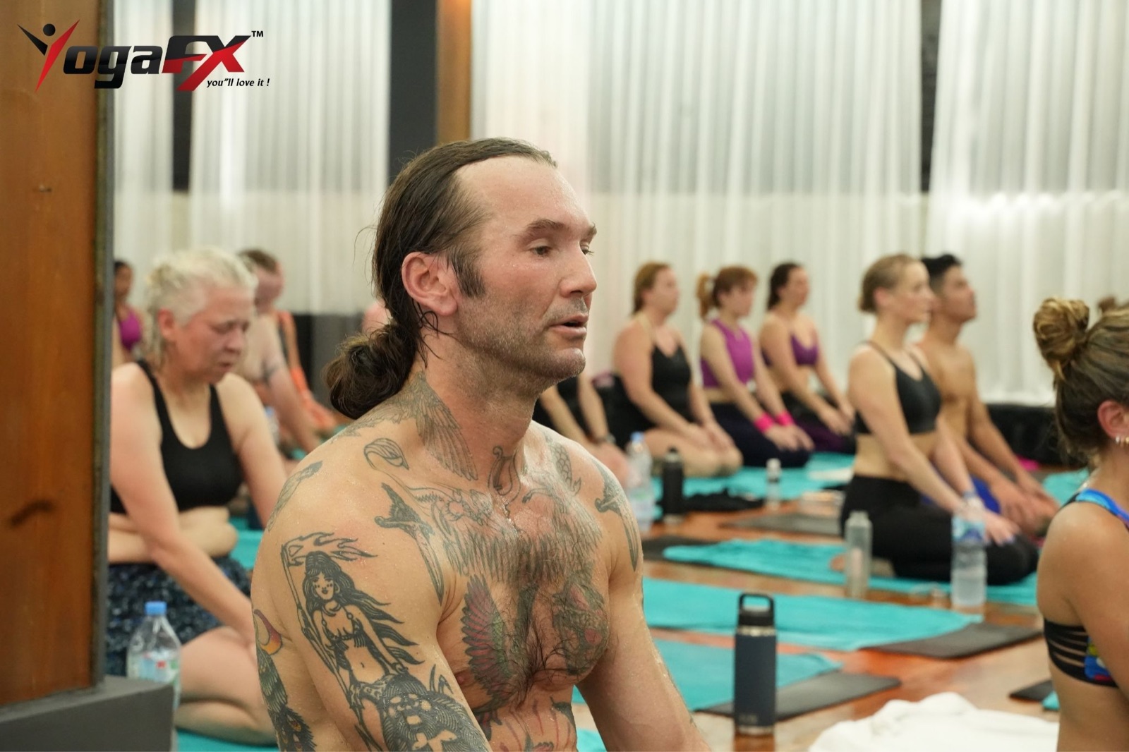A bearded male student seated between other students during a heated 26 and 2 class at the YogaFX studio