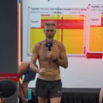 Mr Ian Terry delivering the 26 and 2 dialogue through a microphone in front of the student posture clinic board at YogaFX Bali