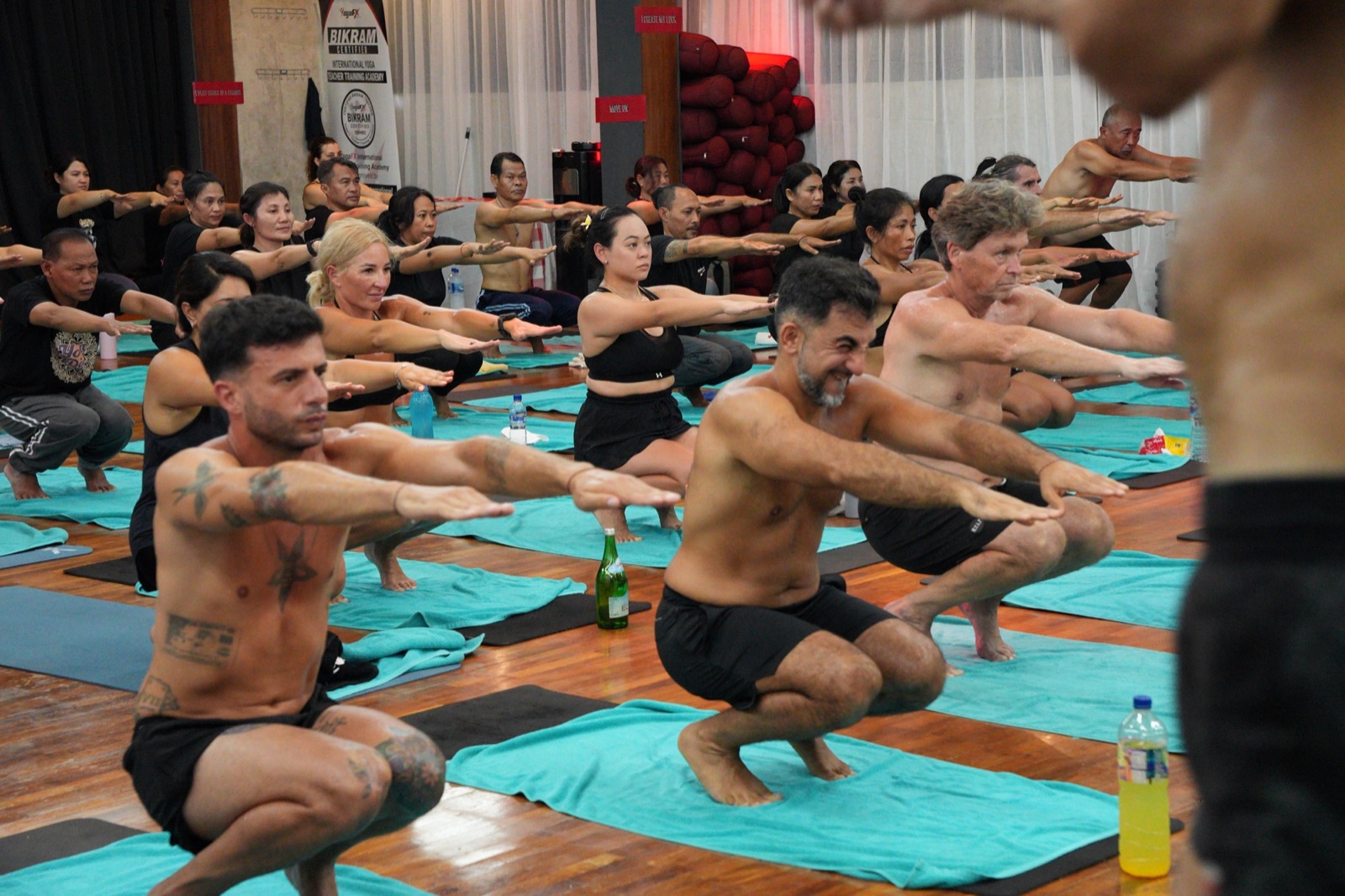 A row of men holding Awkward Pose together in the heated room at the YogaFX studio, sweating through the standing series