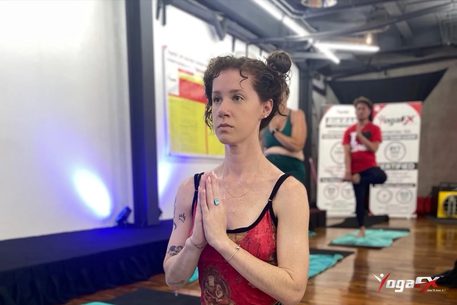 Student standing calm with hands at the heart during the opening of an original hot yoga class